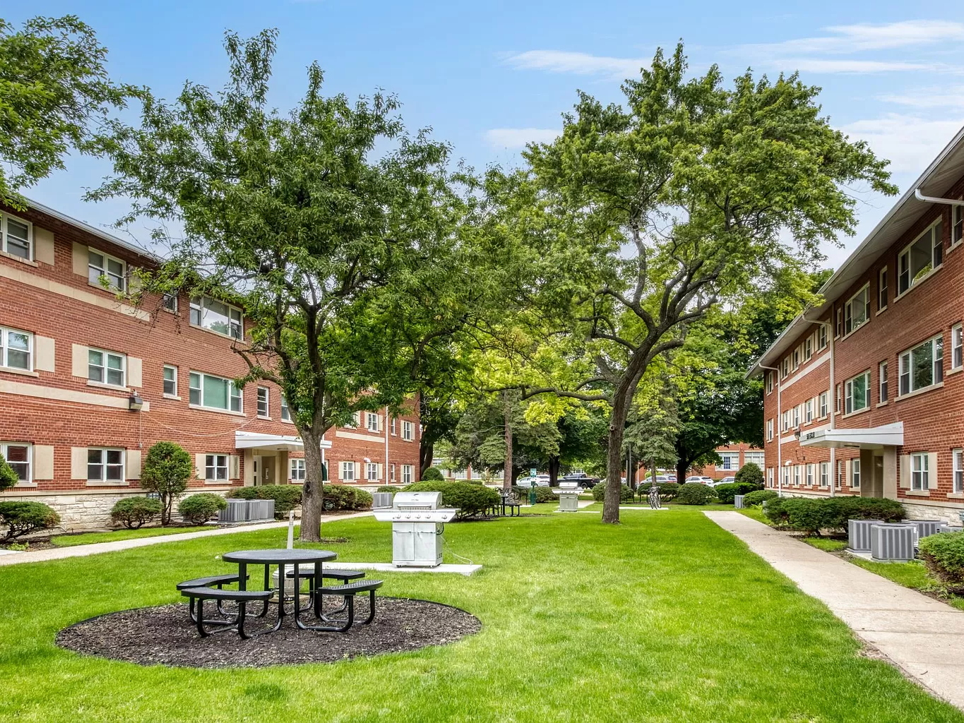 Exterior image of two 3 story residential buildings facing a courtyard with trees. 
