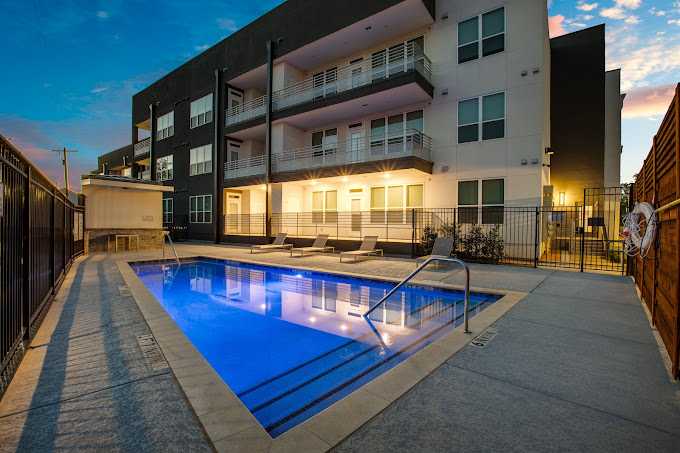 Angular shot of real estate property with a blue lit pool. The sun is setting behind the property with a dark grey and white facade. 