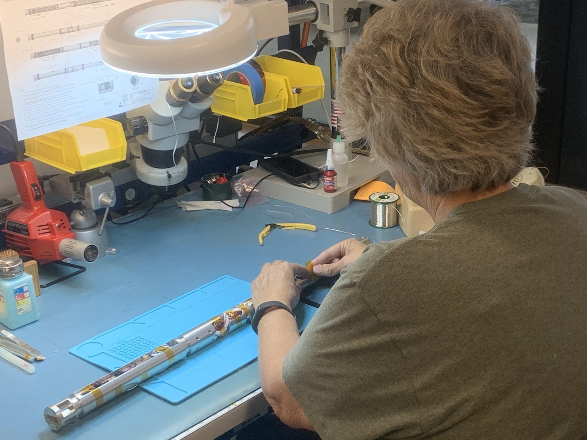 A woman is working on a flute under a magnifying glass.