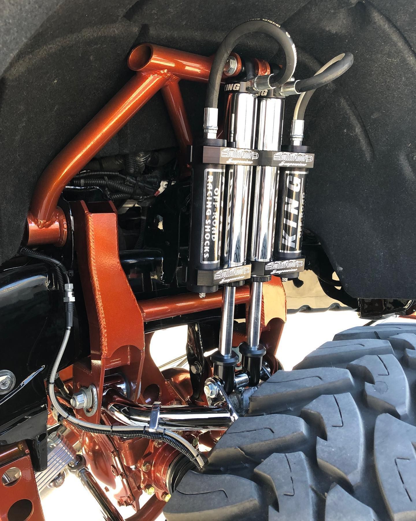 Close-up of a vehicle’s high-performance orange suspension system, including chrome shock absorbers and a rugged tire.