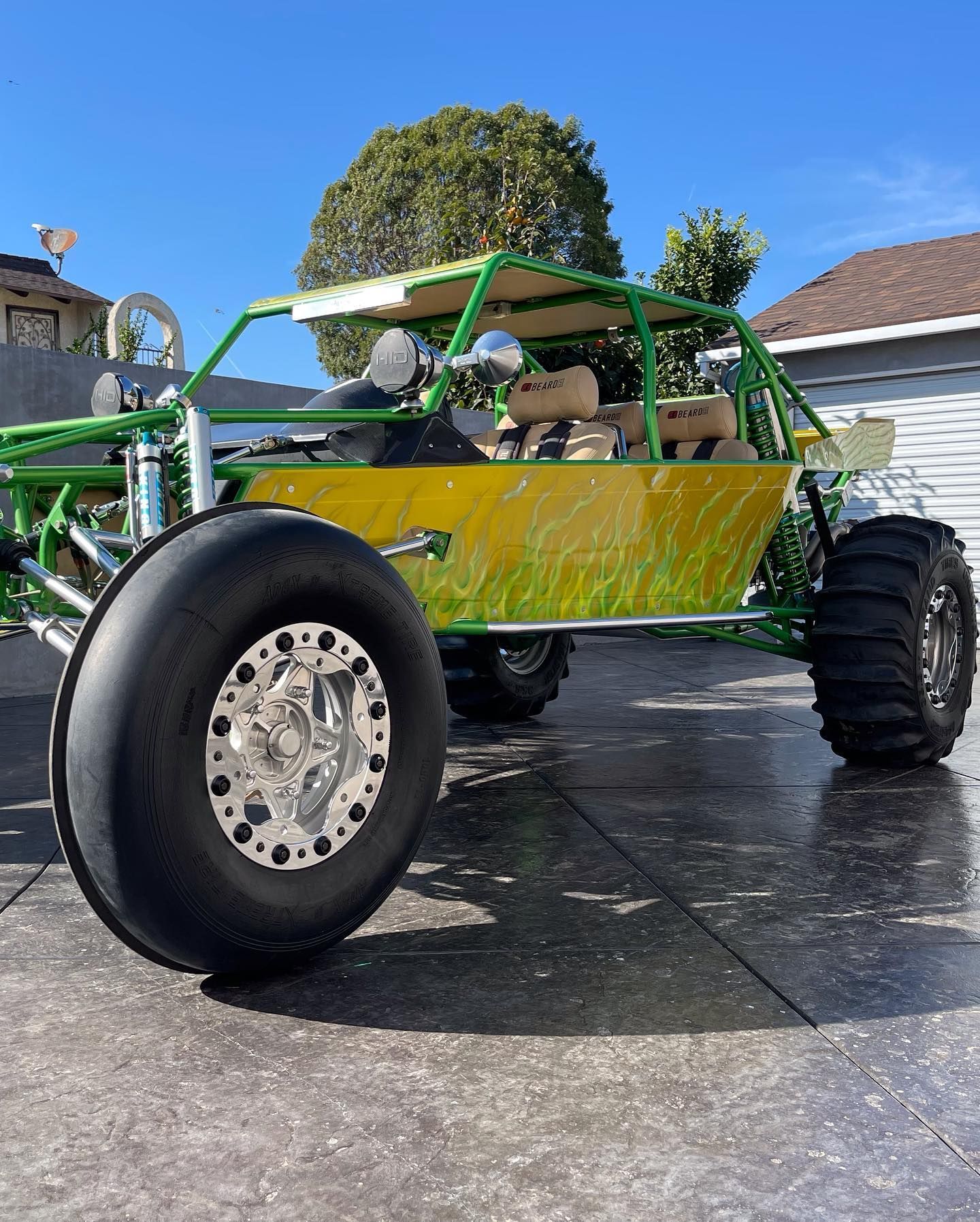 A bright green and yellow off-road sand rail vehicle with large, specialized tires parked on a concrete driveway.