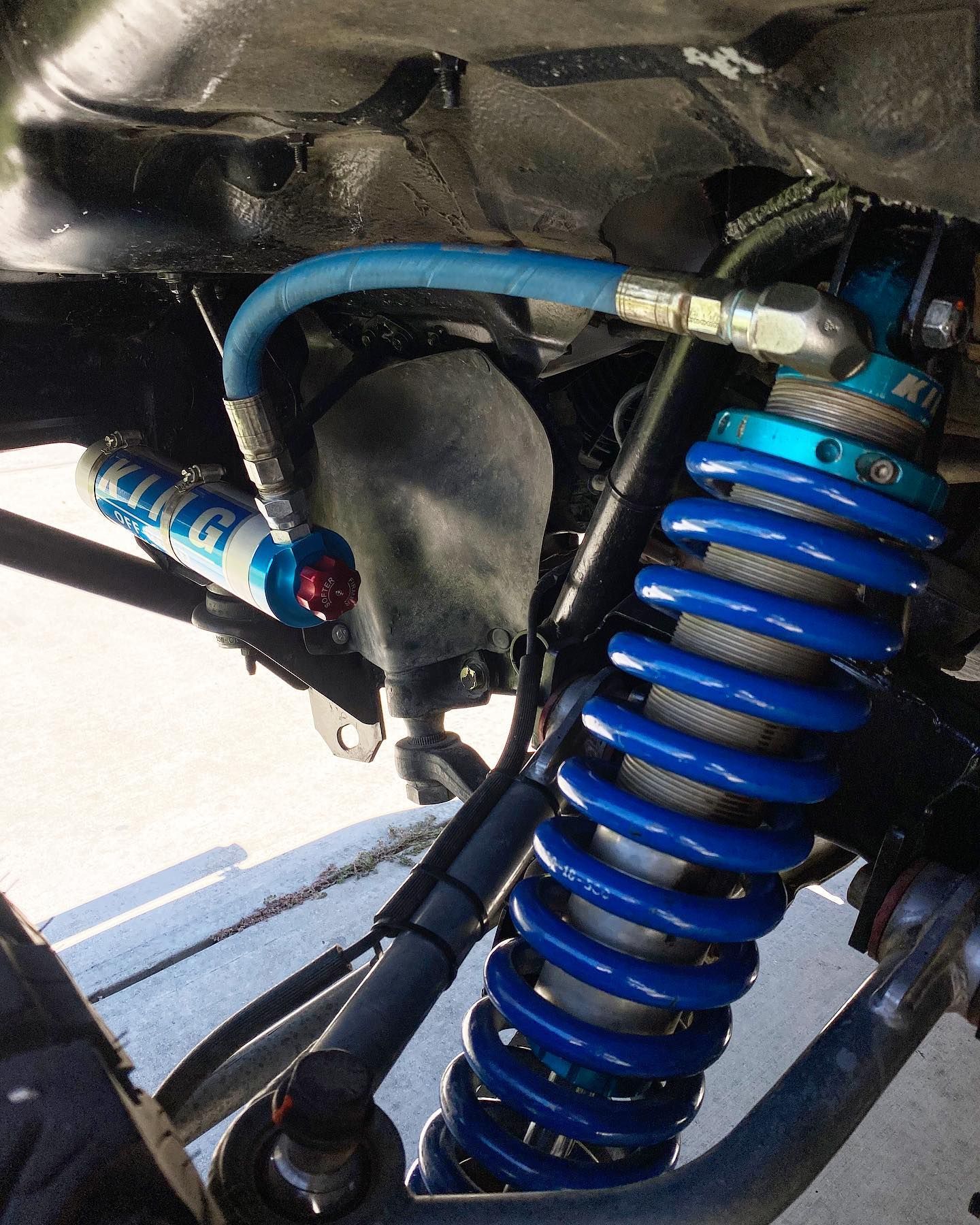 A high-performance King off-road shock absorber with a blue coil spring and remote reservoir mounted on a vehicle.