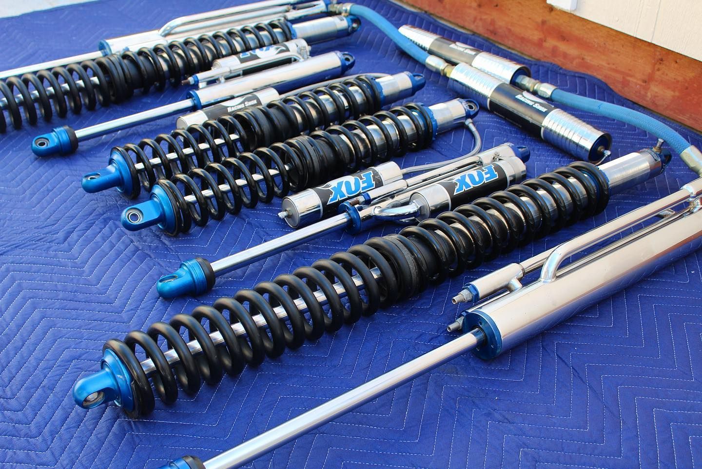 Several high-performance Fox racing shock absorbers with black springs and blue accents displayed on a blue moving blanket.