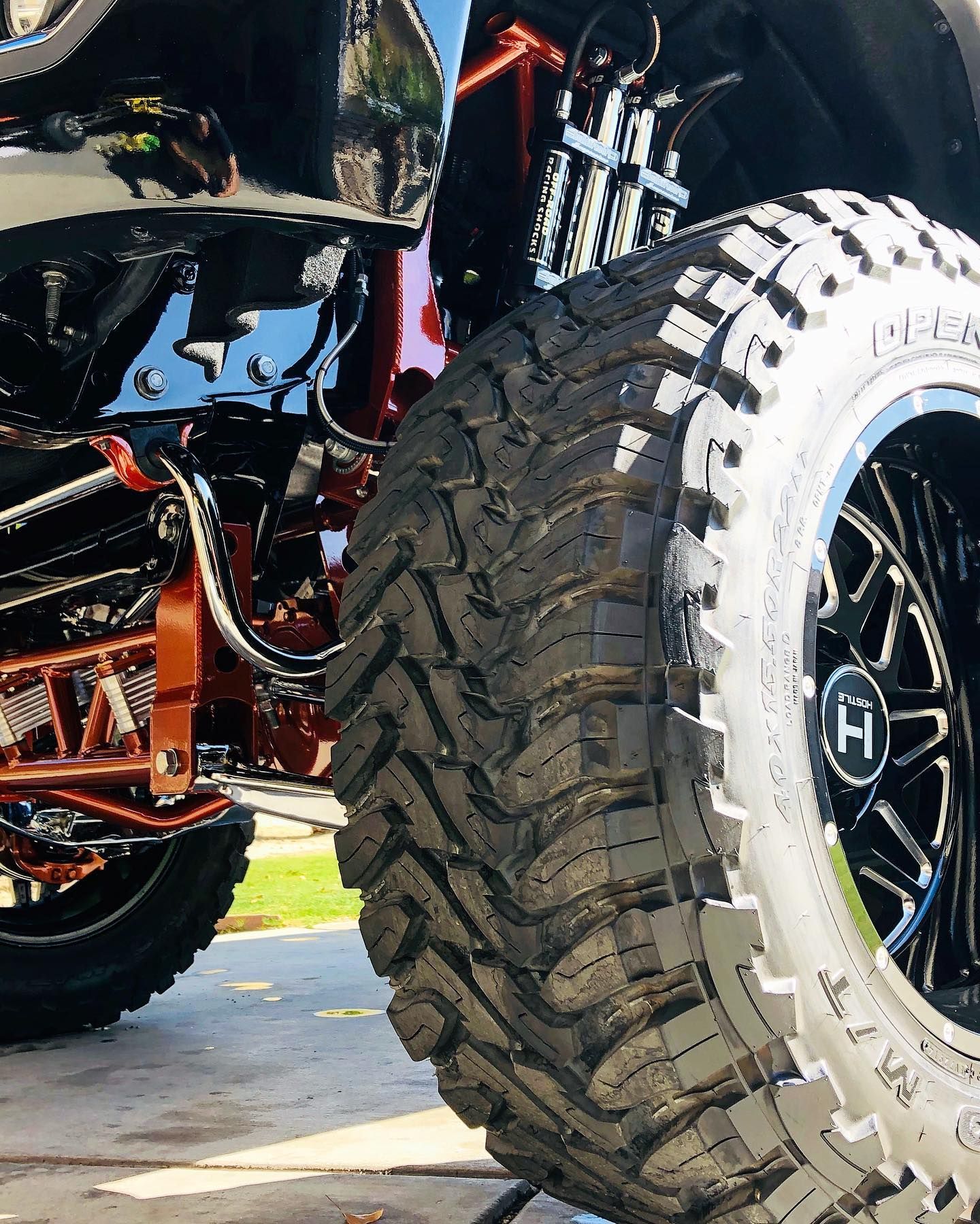 A close-up of a truck's large off-road tire with a custom black wheel, featuring a bright orange suspension system.