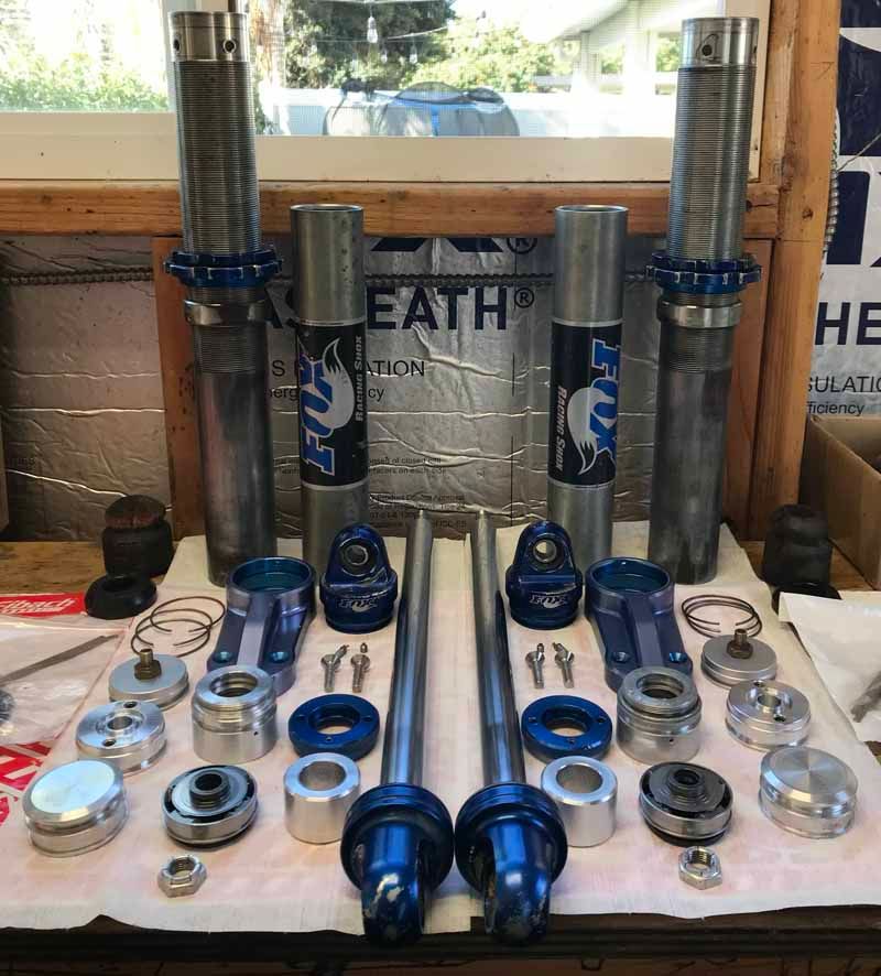 Disassembled Fox racing shock absorbers and various blue and metal components laid out on a workbench.
