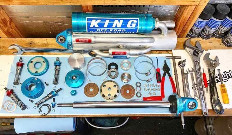 A King off-road racing shock absorber disassembled on a workbench with various metal components and shop tools.