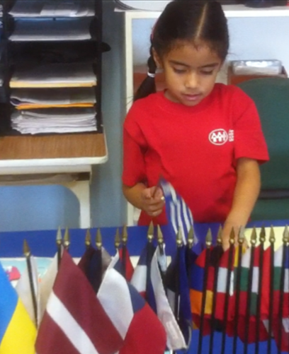A little girl in a red shirt is standing in front of a table full of small flags