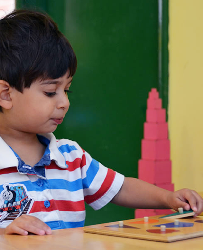 A young boy in a striped shirt is playing with a puzzle on a table.