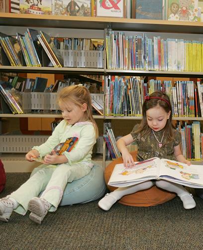 Two little girls are reading books in a library