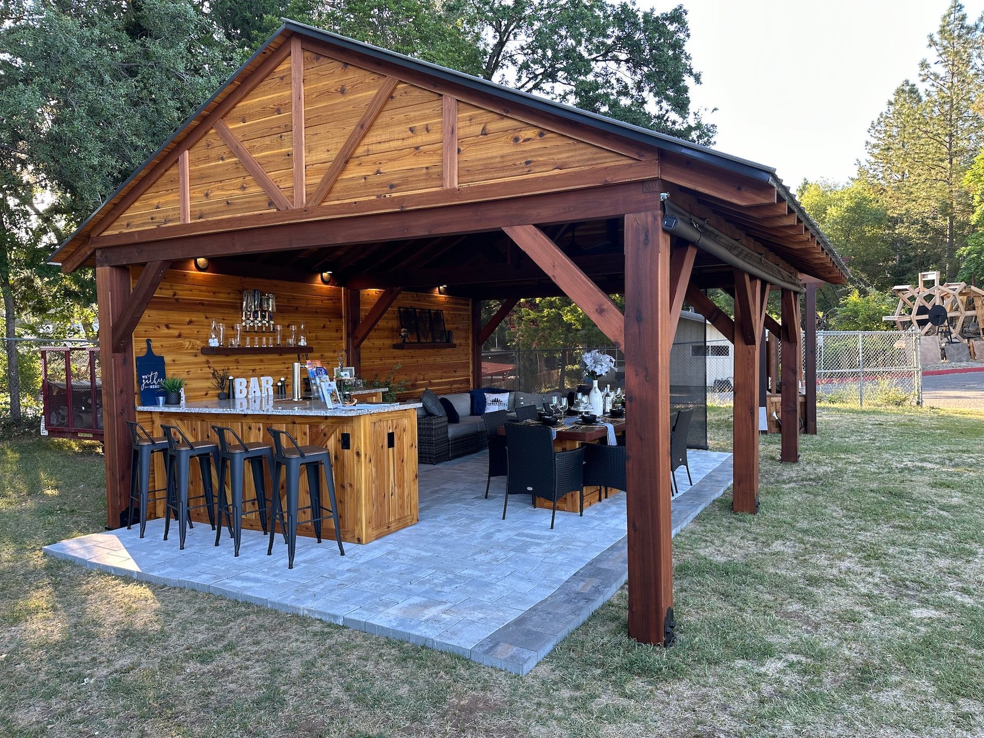 A wooden pavilion with a bar and stools in the middle of a field.