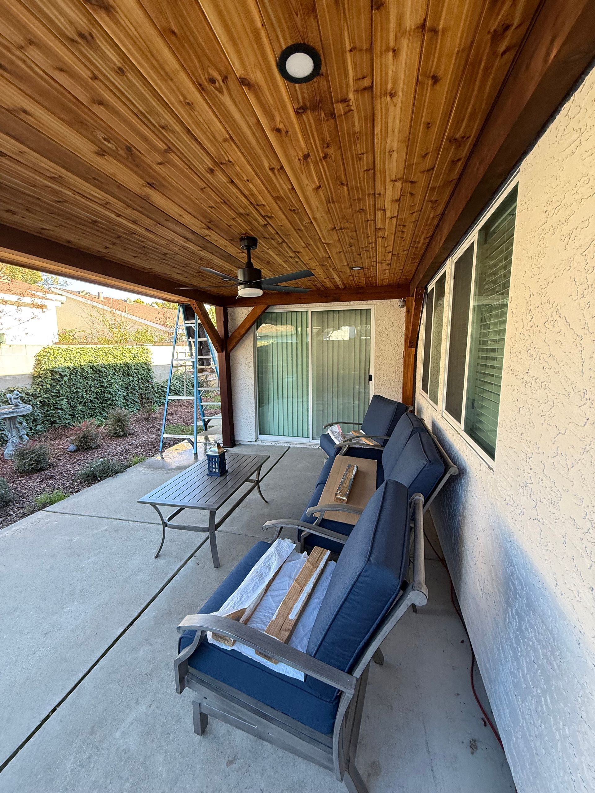 Patio with wood ceiling, blue chairs, and a table. A sliding glass door is visible.