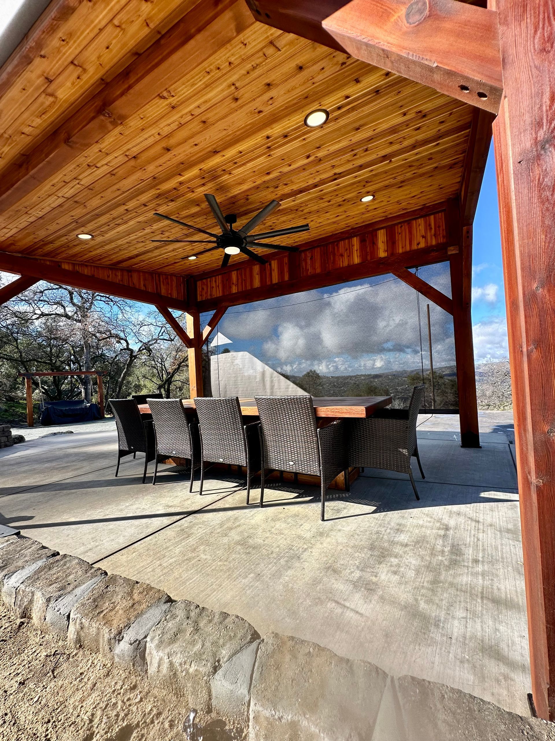 A wooden patio cover with a ceiling fan and a table and chairs underneath it.