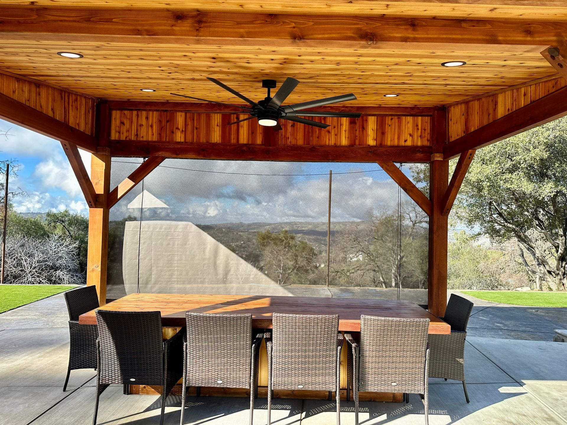 A wooden patio cover with a table and chairs and a ceiling fan