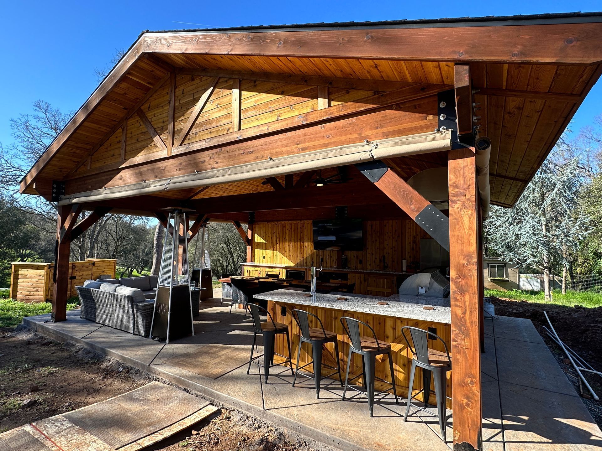 A wooden pavilion with a bar and chairs underneath it.