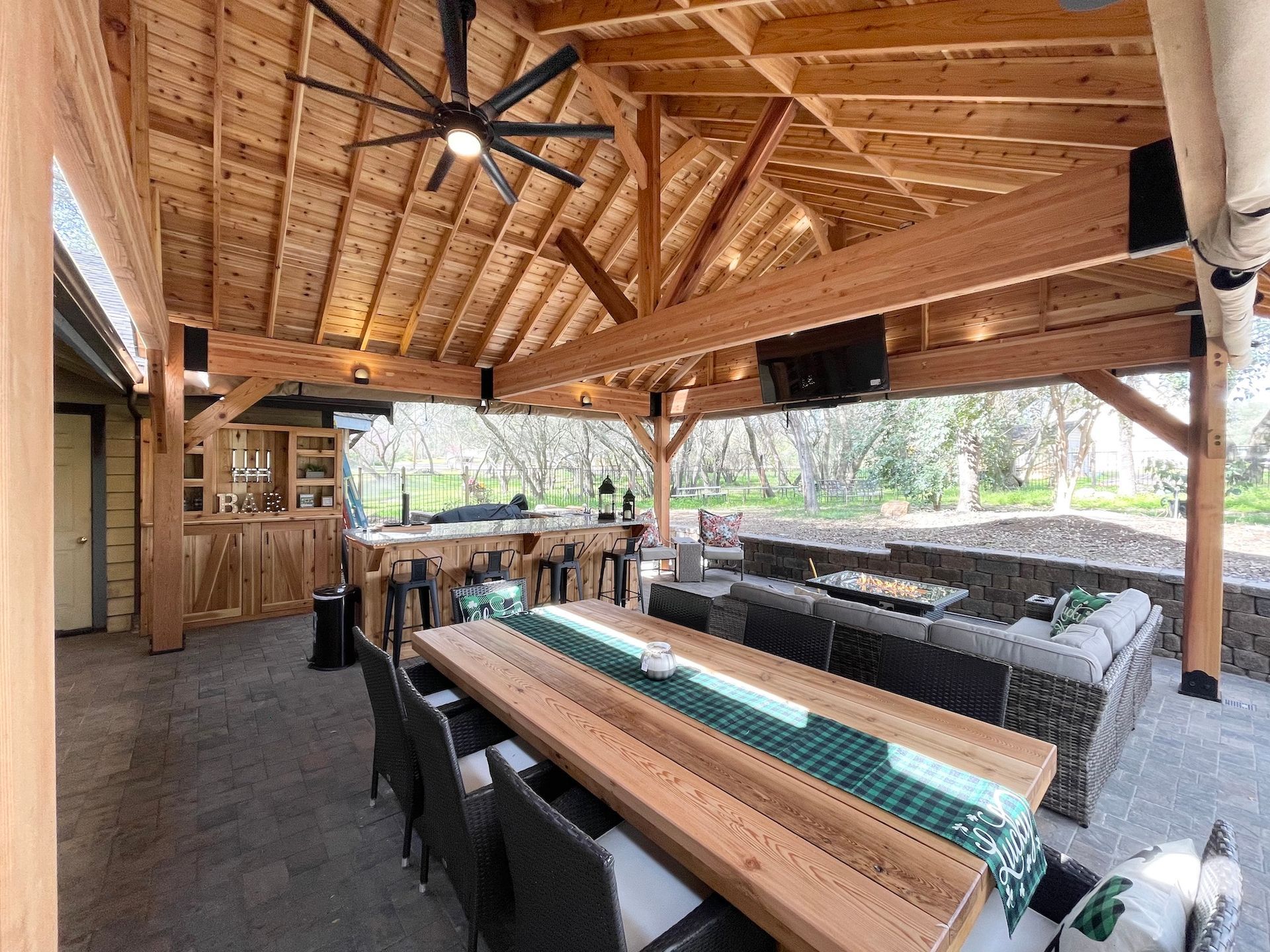 A large wooden table and chairs under a wooden roof.