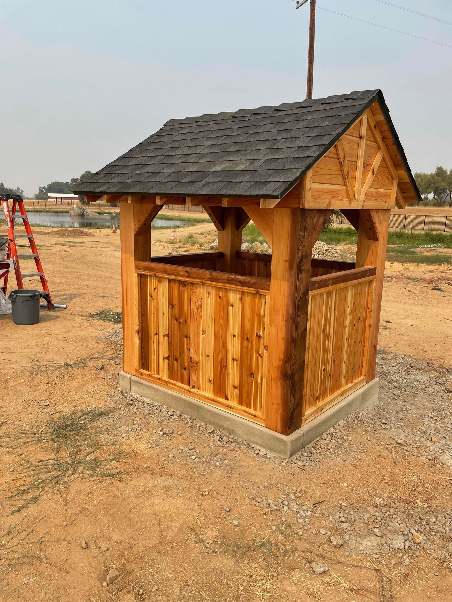 A small wooden shed with a black roof is sitting in the middle of a dirt field.