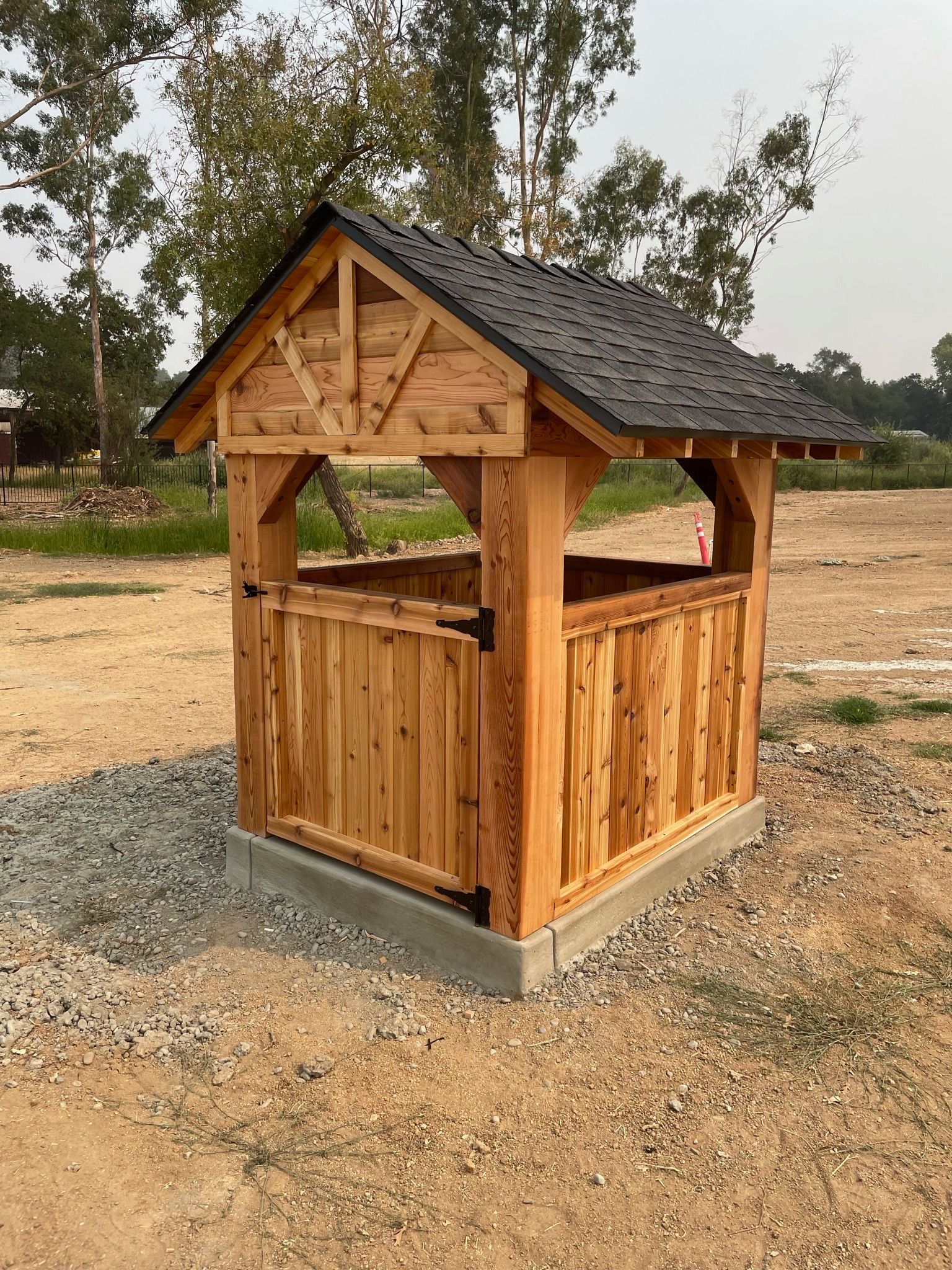 A small wooden shed with a black roof is sitting in the middle of a dirt field.