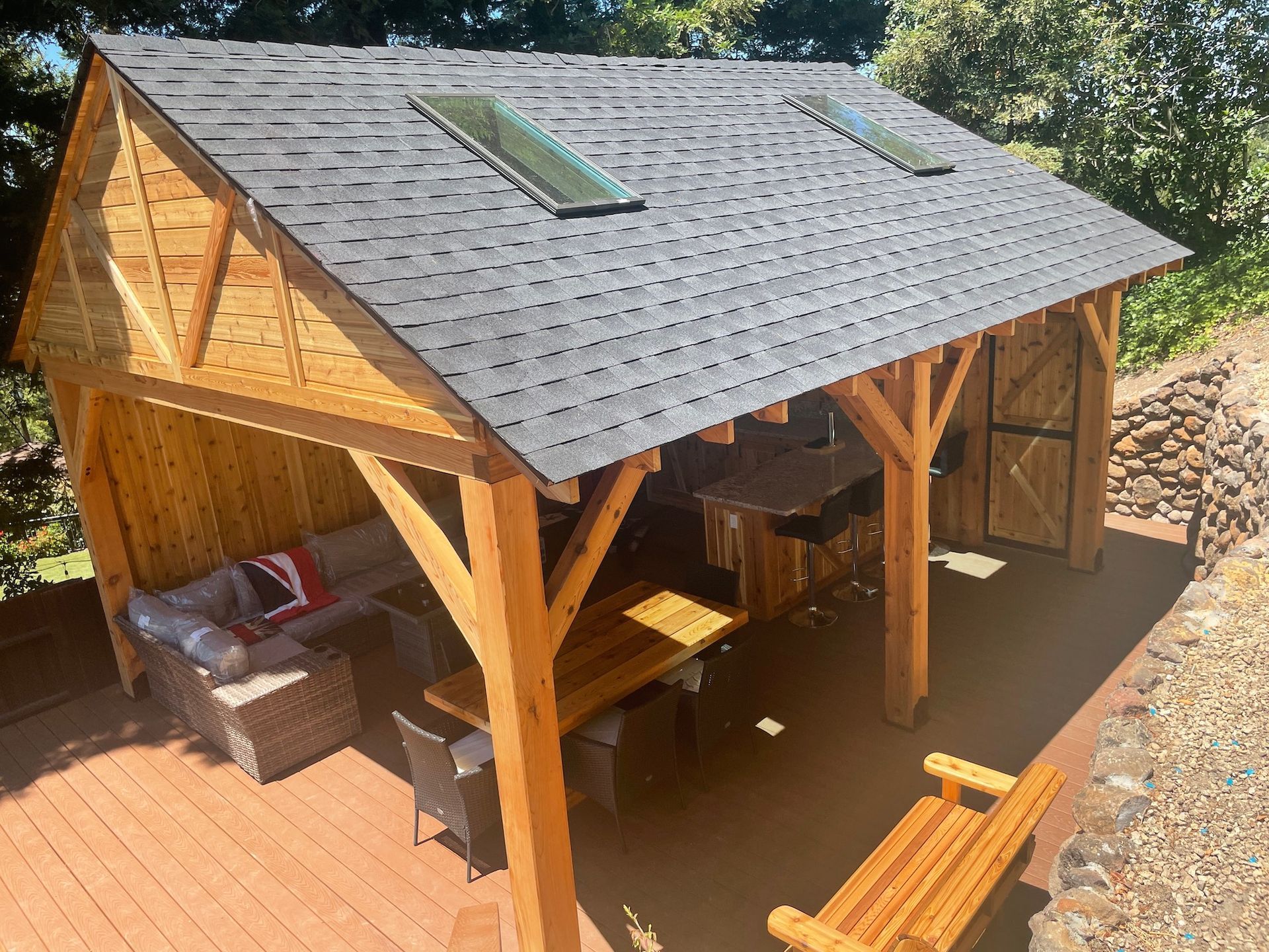 A wooden pavilion with a slate roof and a table and chairs underneath it.