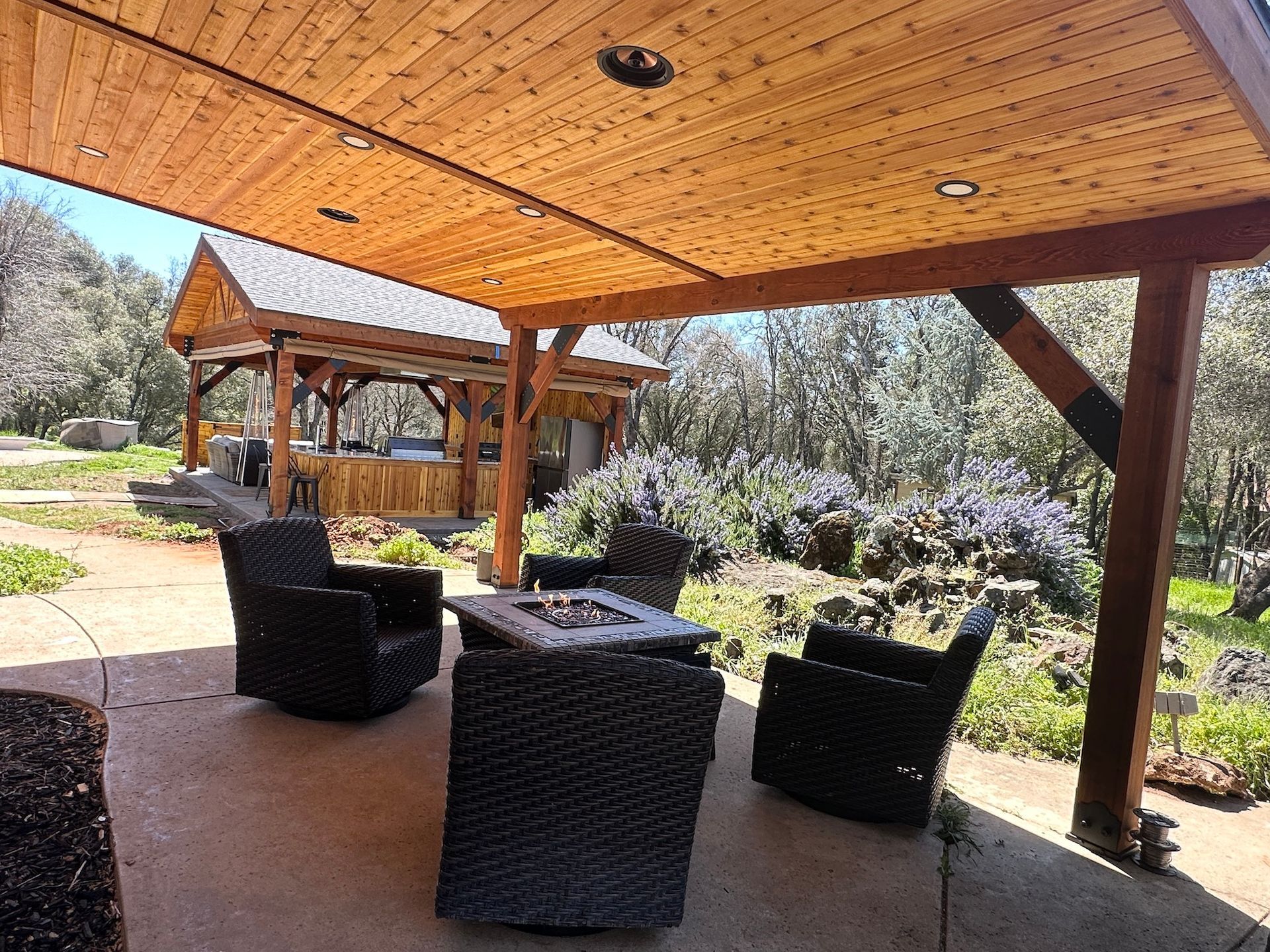 A patio with chairs and a fire pit under a wooden roof.