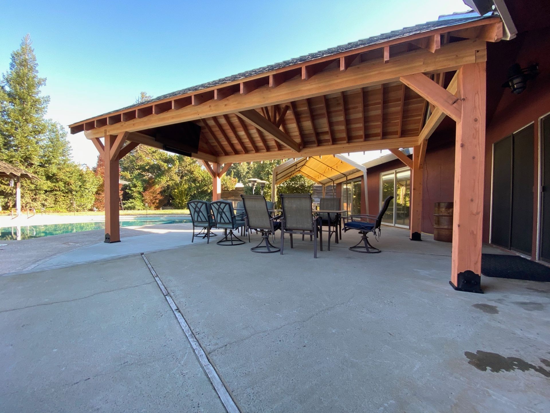 A patio with a table and chairs under a wooden roof.