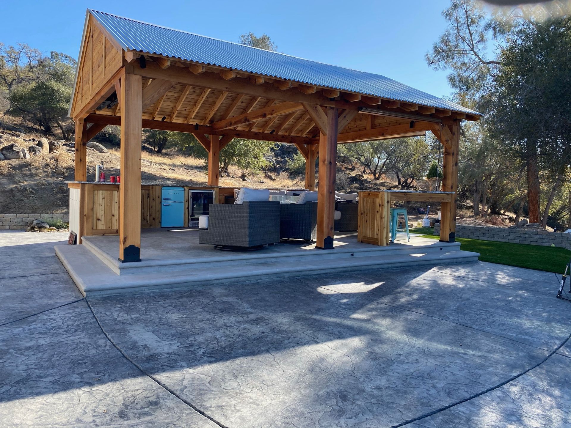 A large wooden pavilion with a metal roof is sitting in the middle of a driveway.