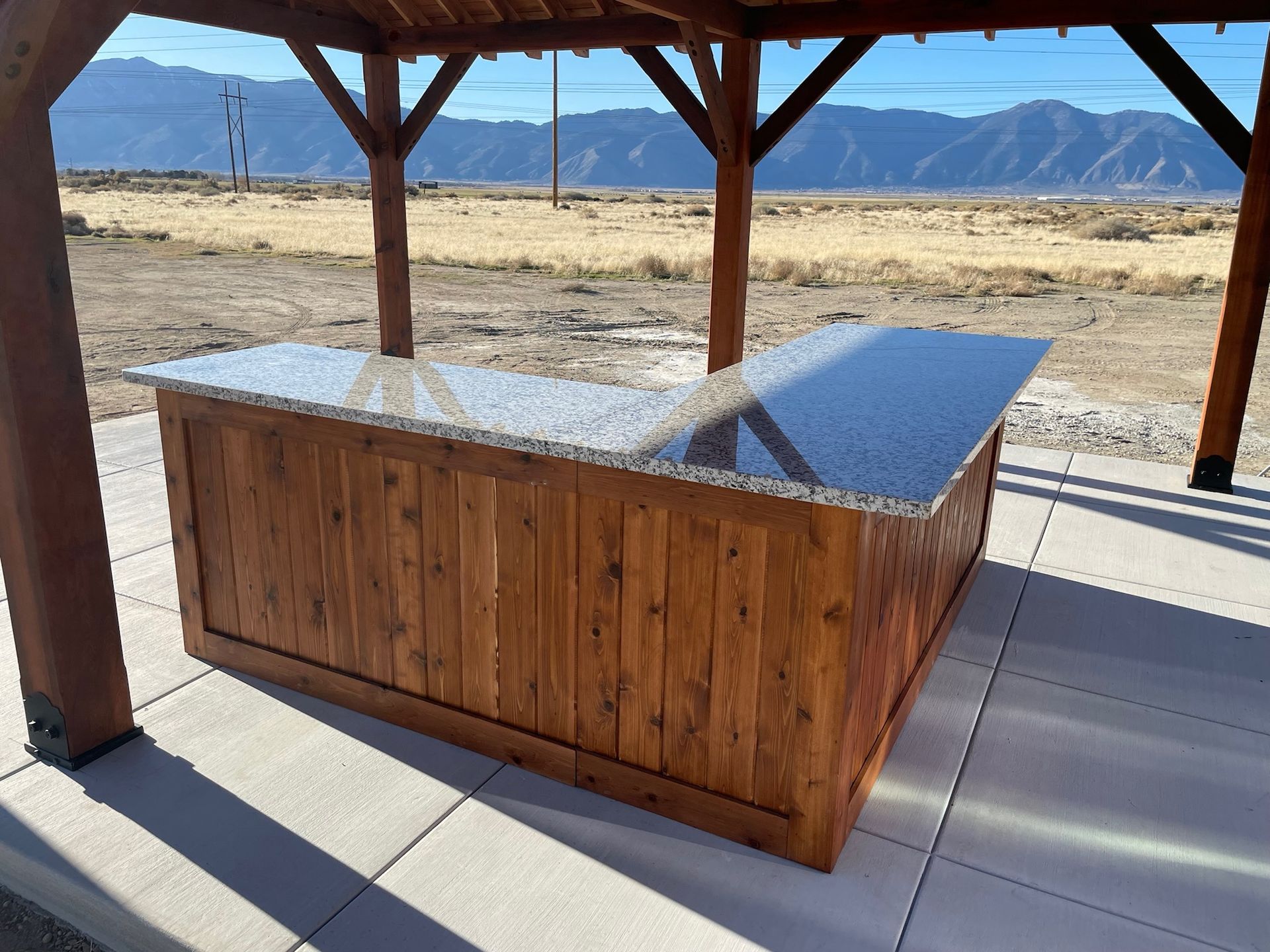 A wooden table with a granite counter top under a wooden structure.