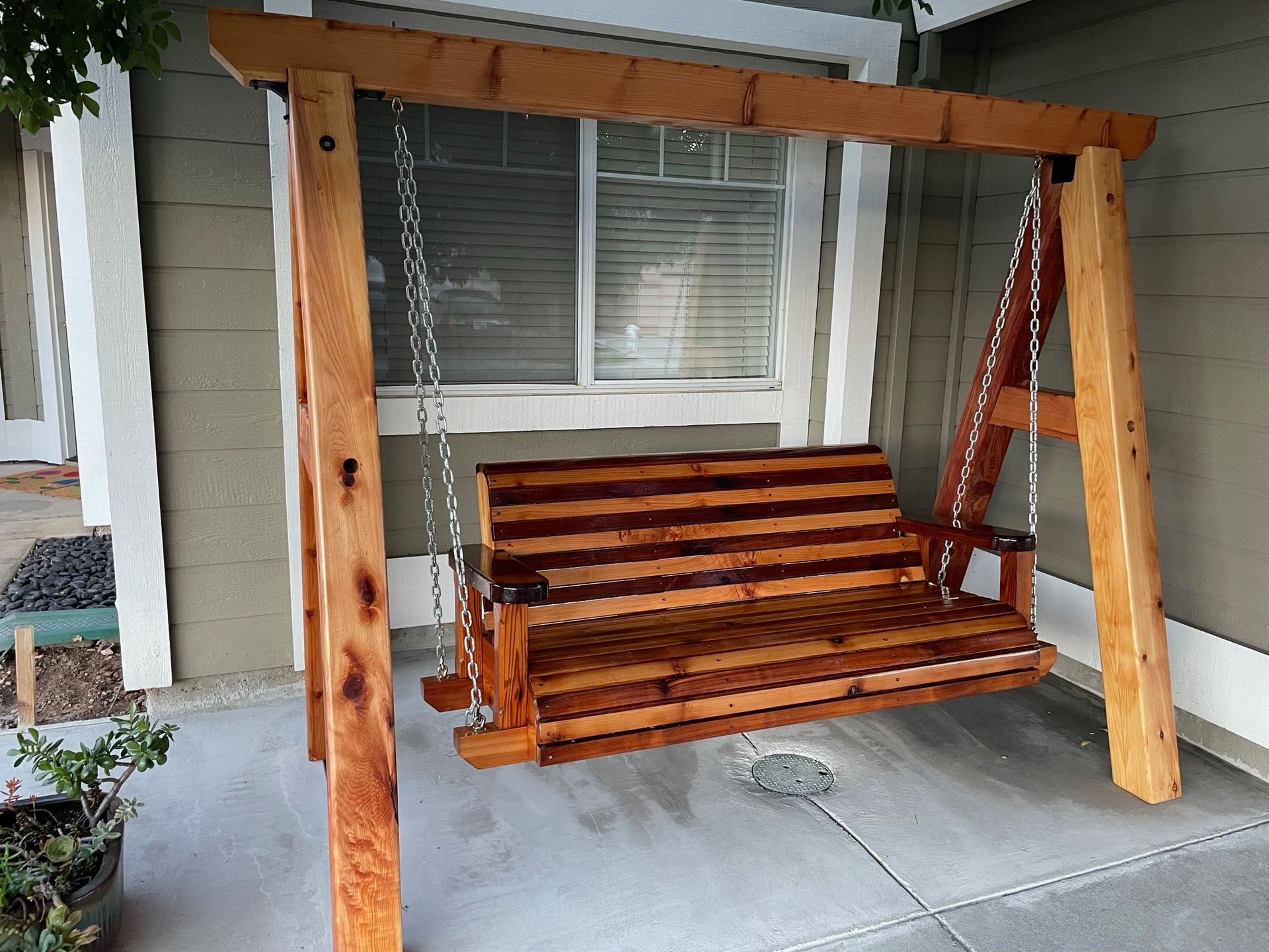 A wooden swing is sitting in front of a house.