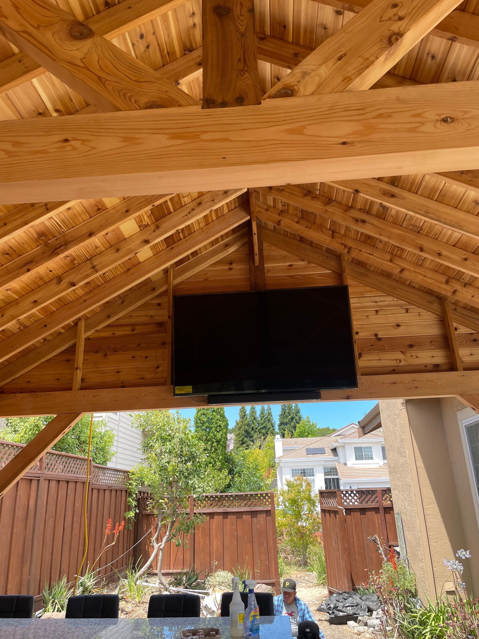 A large flat screen tv is hanging from the ceiling of a wooden structure.