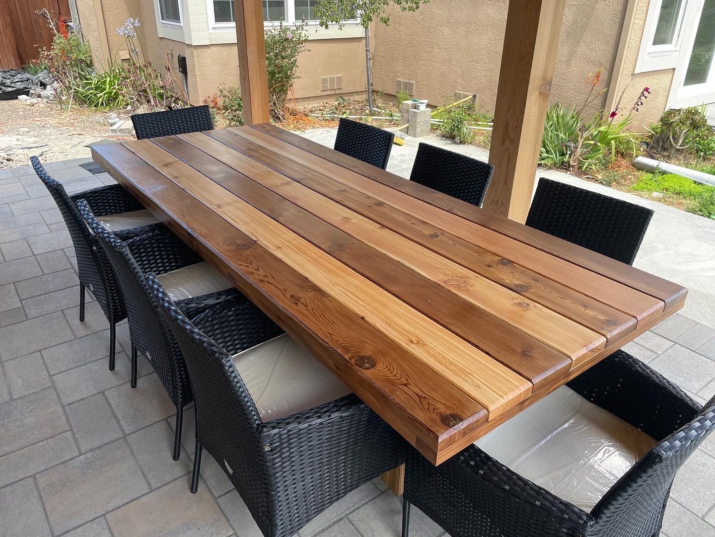 A wooden table with wicker chairs underneath it on a patio.