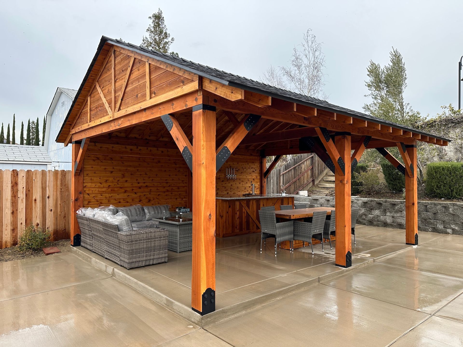 A wooden pavilion with a couch , table and chairs underneath it.