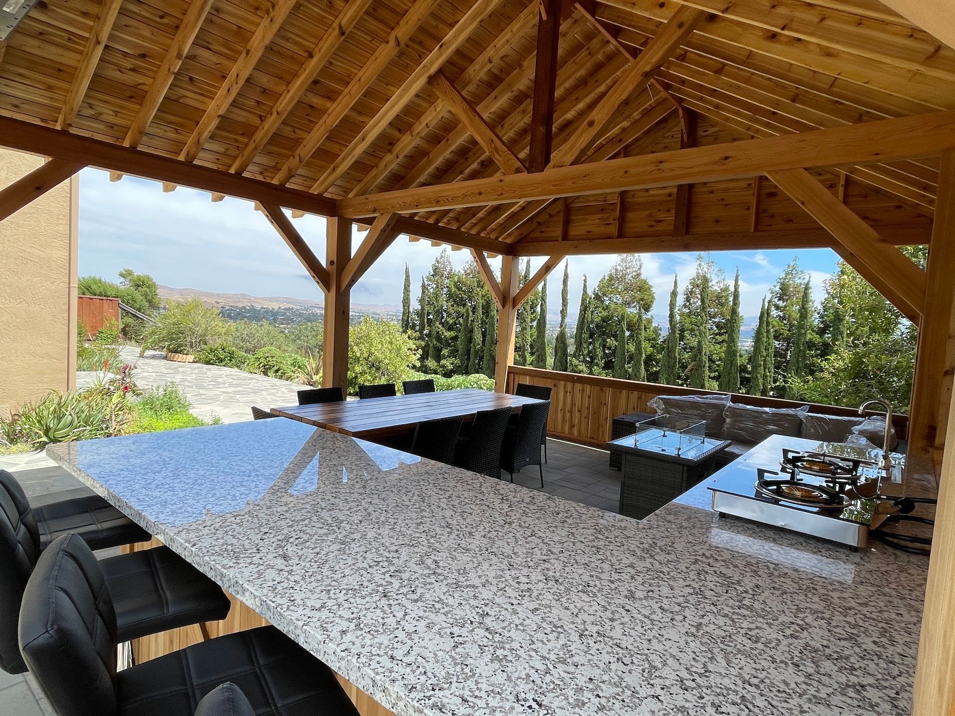 A gazebo with a long table and chairs under a wooden roof.