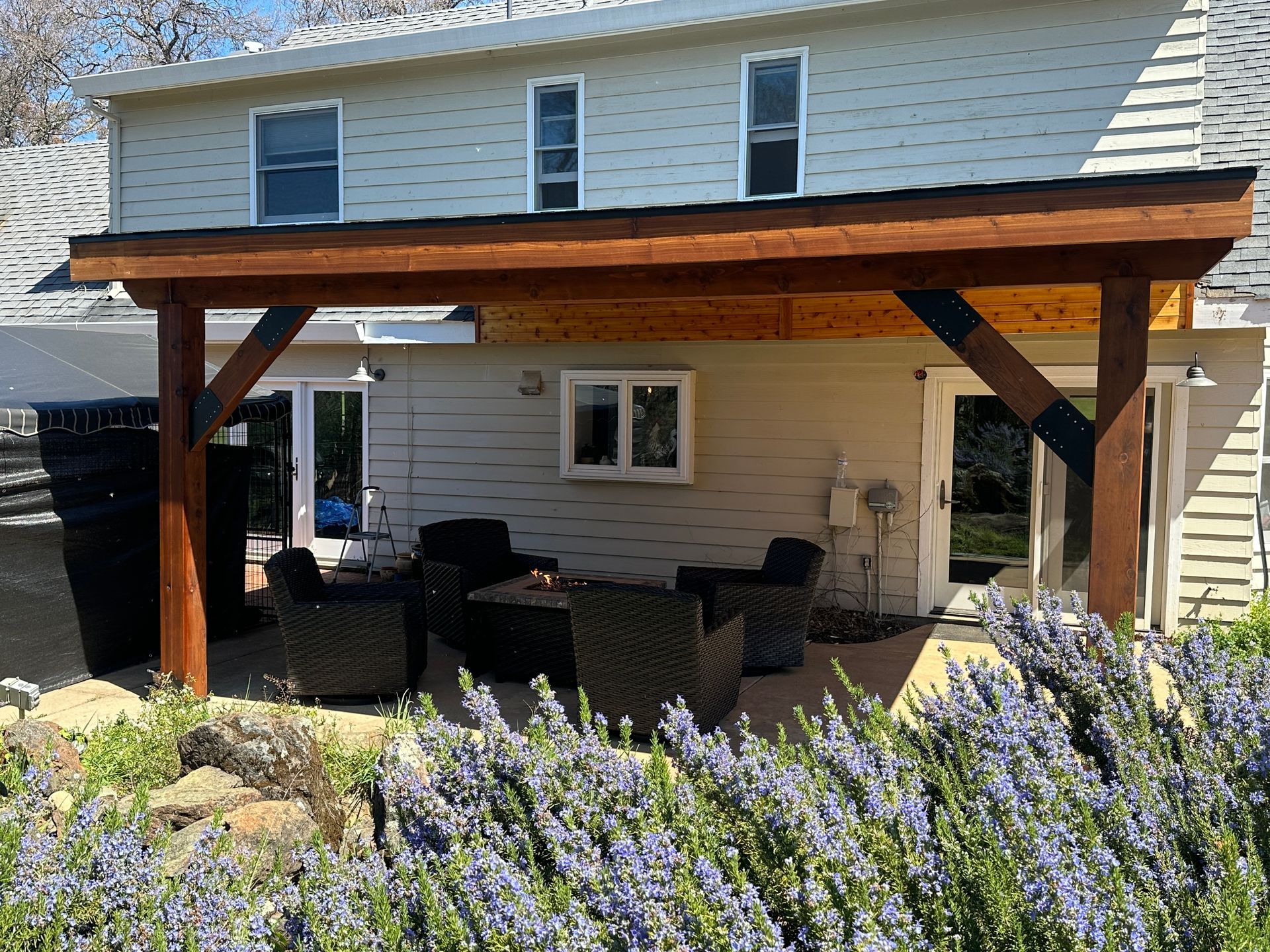 A white house with a wooden covered patio with chairs and a table.