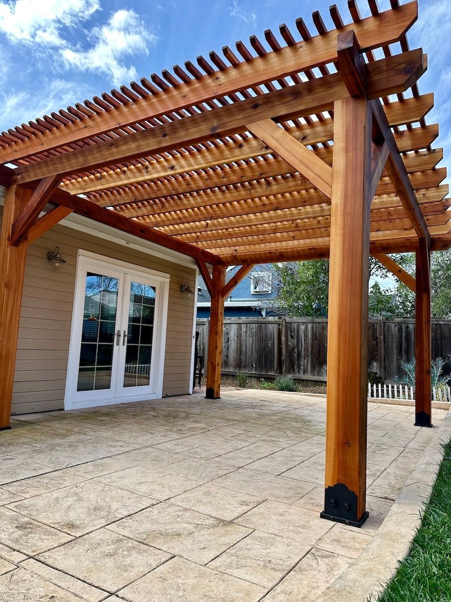A wooden pergola is sitting on top of a patio in front of a house.