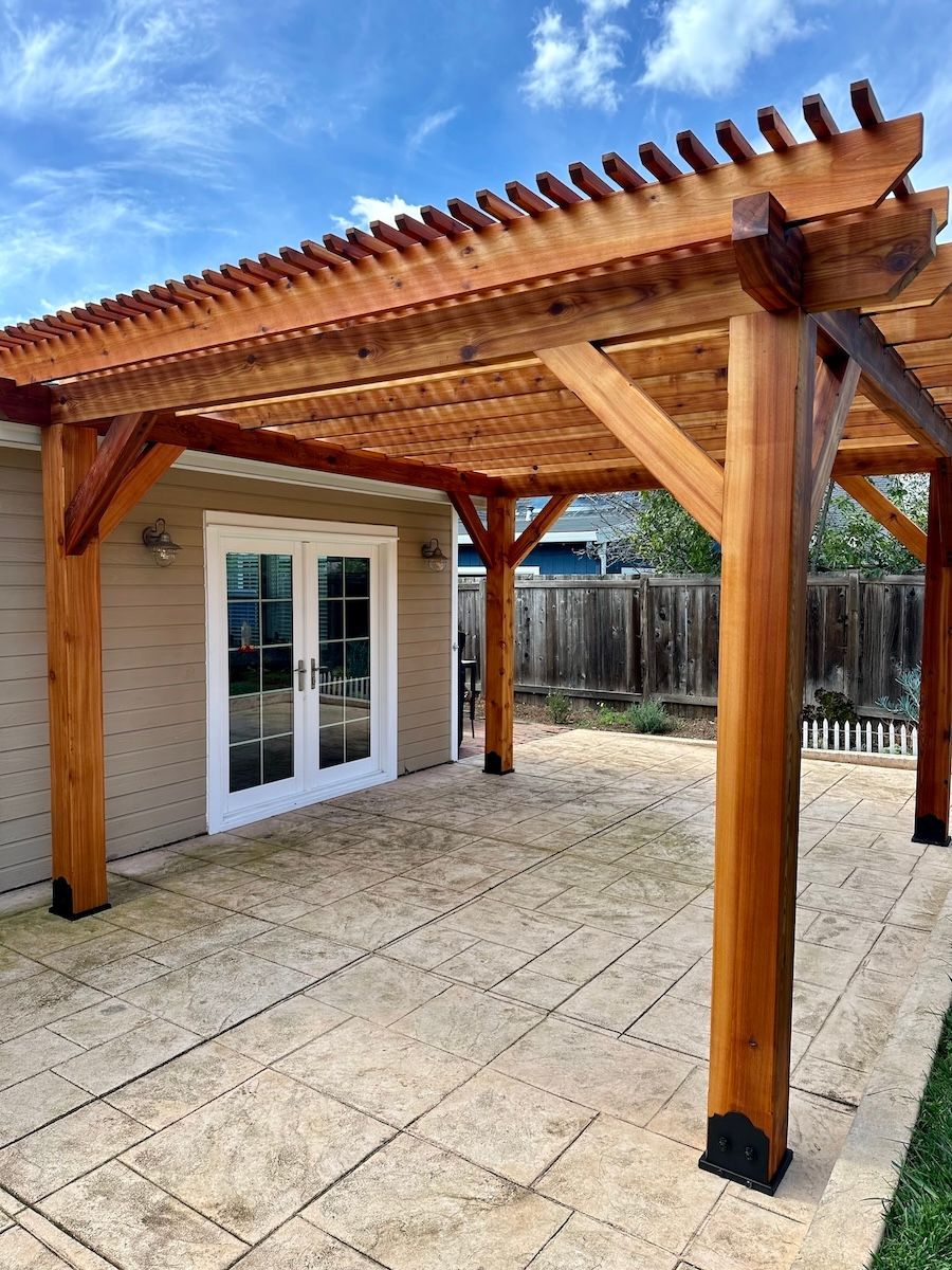 A wooden pergola is sitting on top of a patio in front of a house.