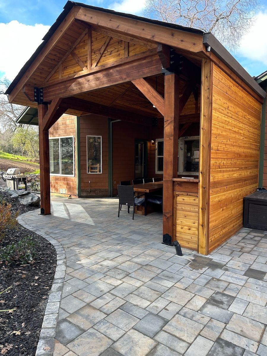 A wooden pavilion with a brick patio in front of it.