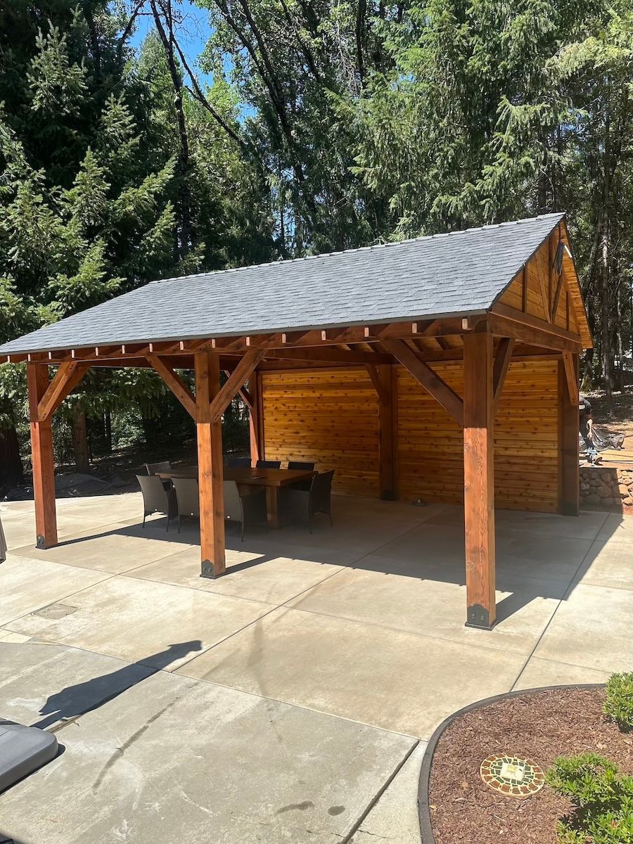 A wooden pavilion with a slate roof is sitting on top of a concrete driveway.
