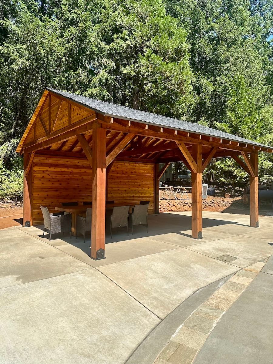 A wooden pavilion with a table and chairs inside of it.