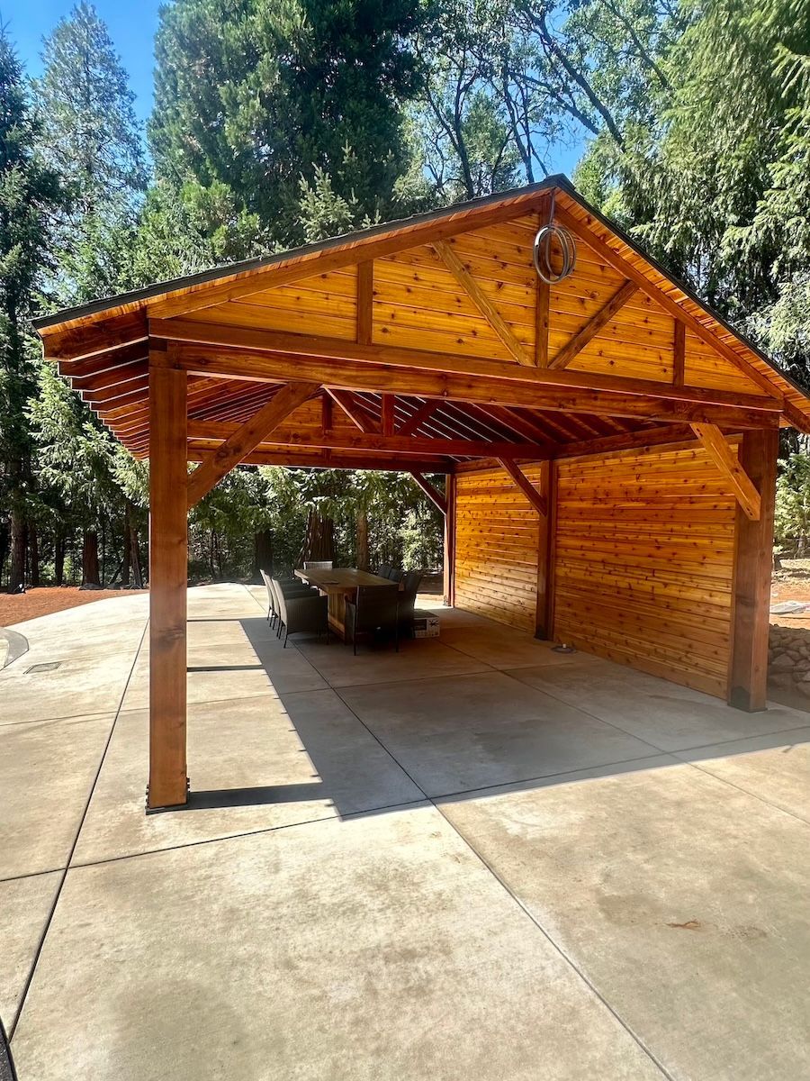 A wooden pavilion with a table and chairs underneath it.