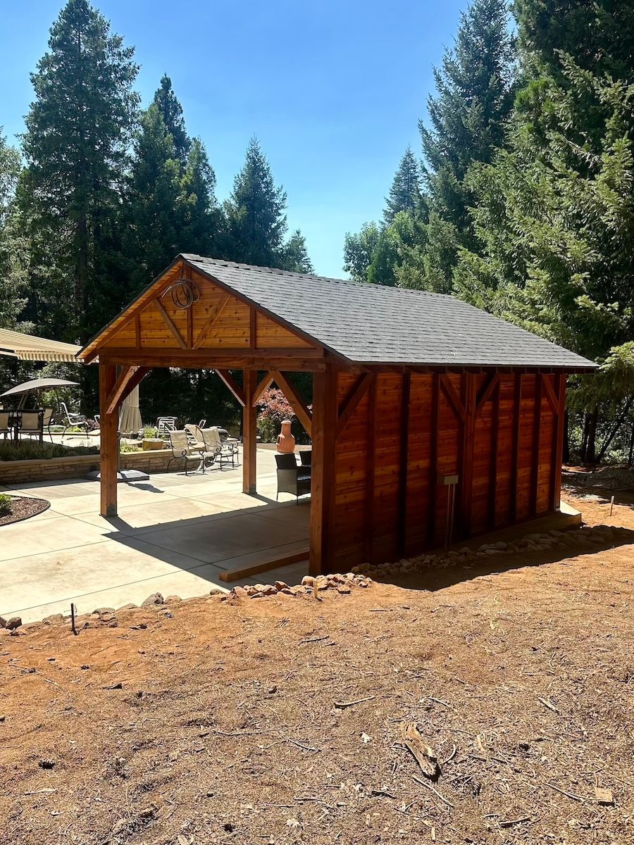 A wooden shed is sitting in the middle of a dirt field surrounded by trees.