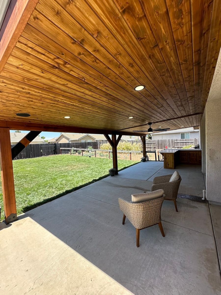 A large covered patio with a wooden ceiling and chairs.