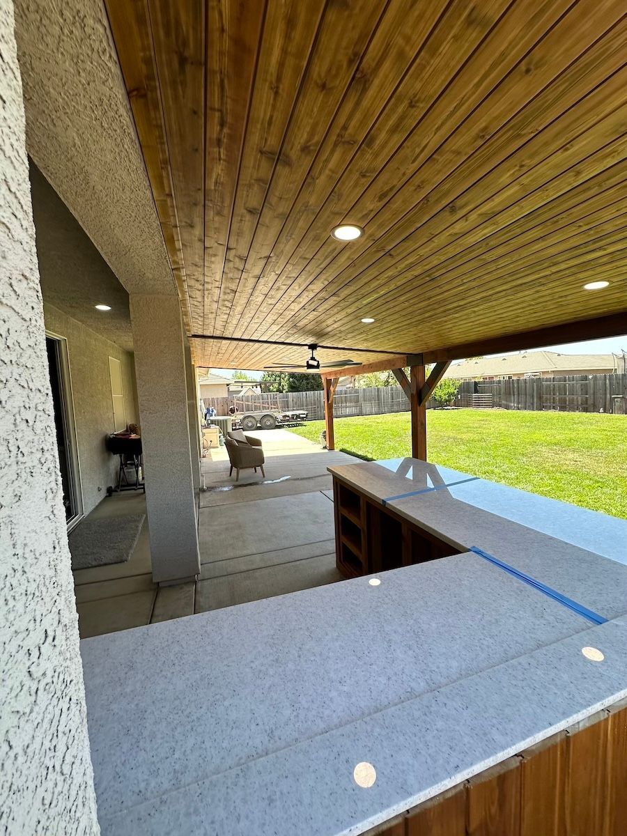 A patio with a wooden ceiling and a ceiling fan.