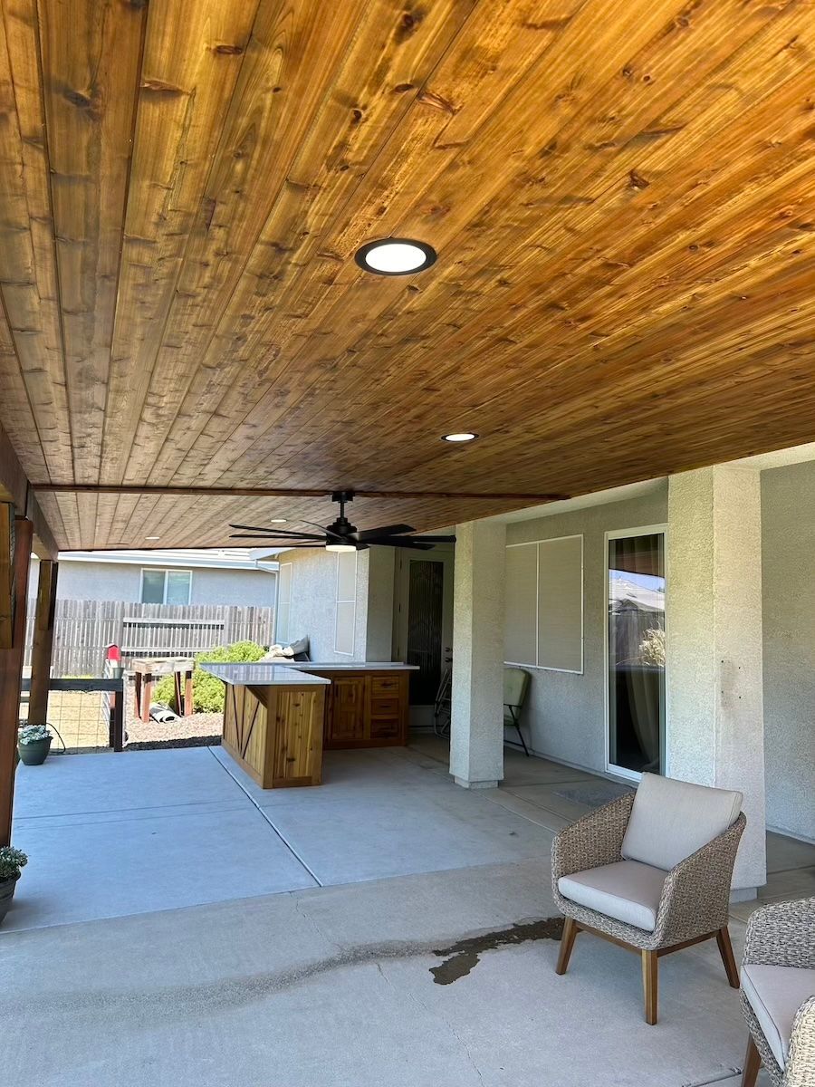 A patio with a wooden ceiling and a ceiling fan.