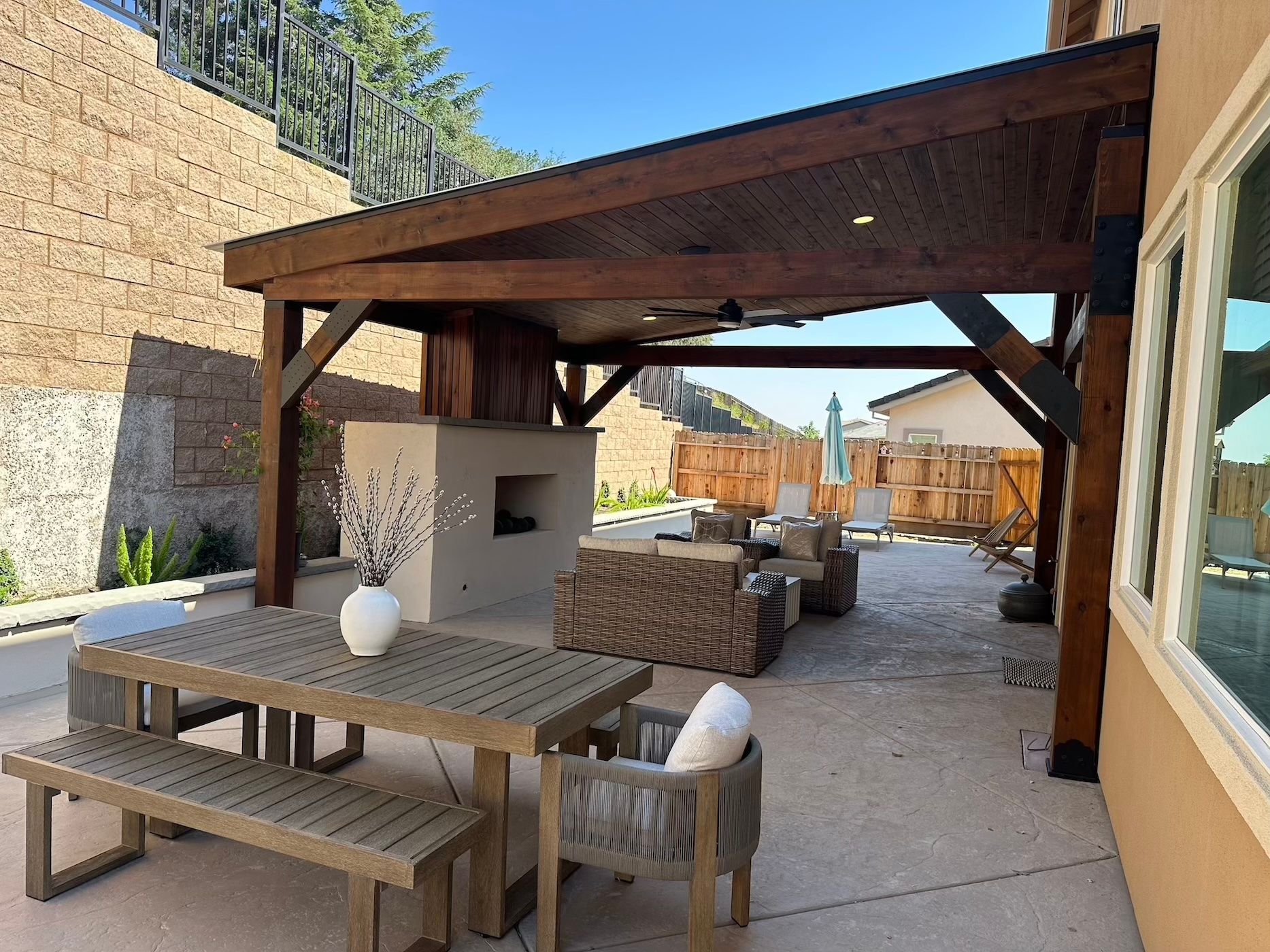 A patio with a table and chairs under a wooden structure
