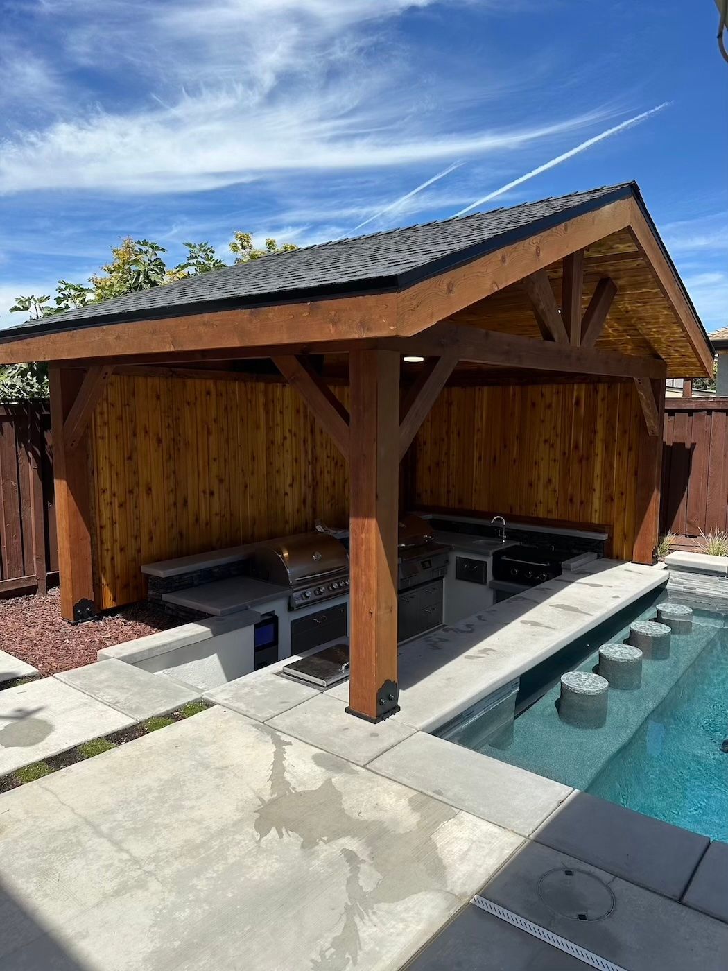 A wooden pavilion is sitting next to a swimming pool.