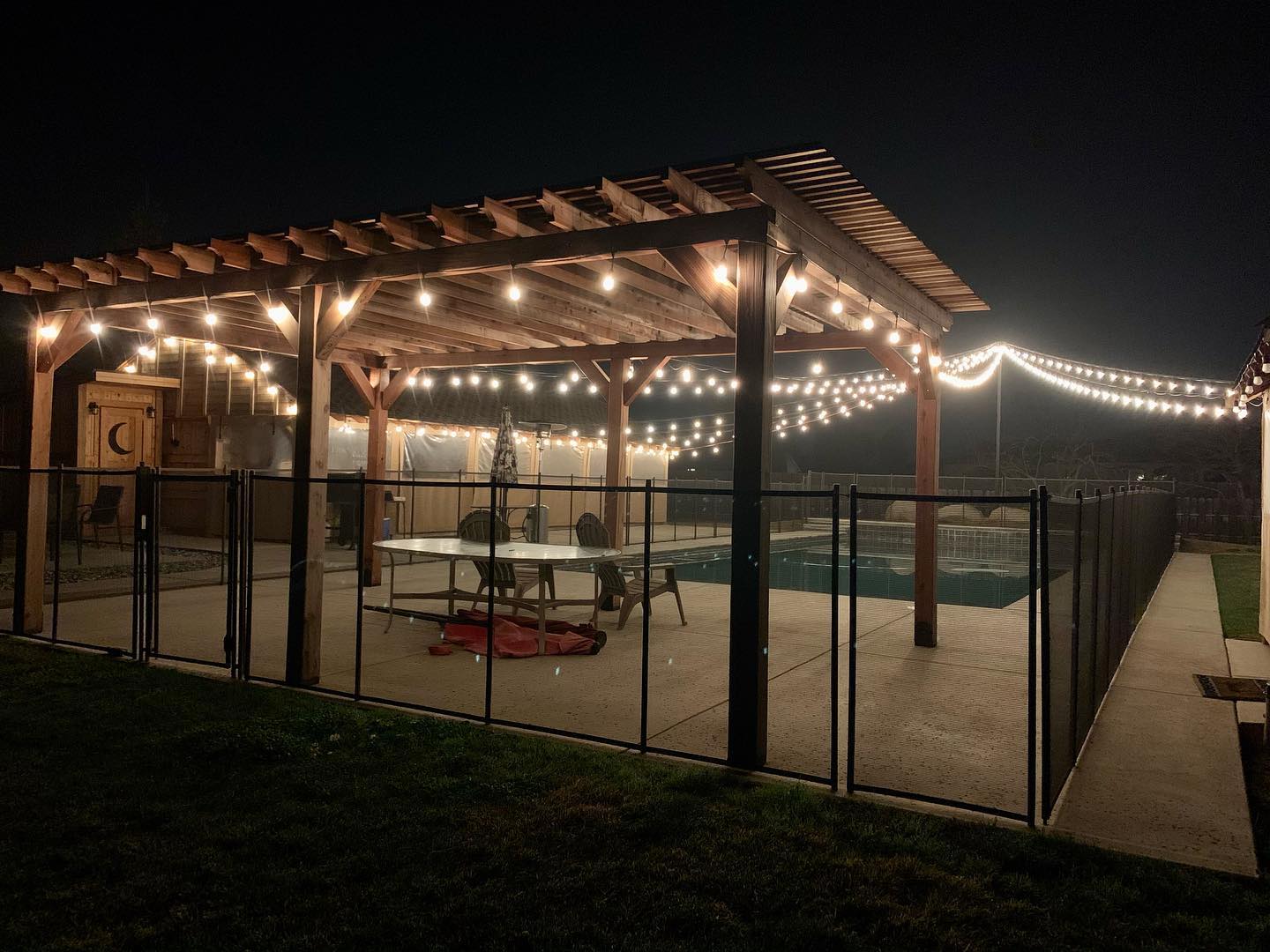 a pergola is lit up at night next to a pool .