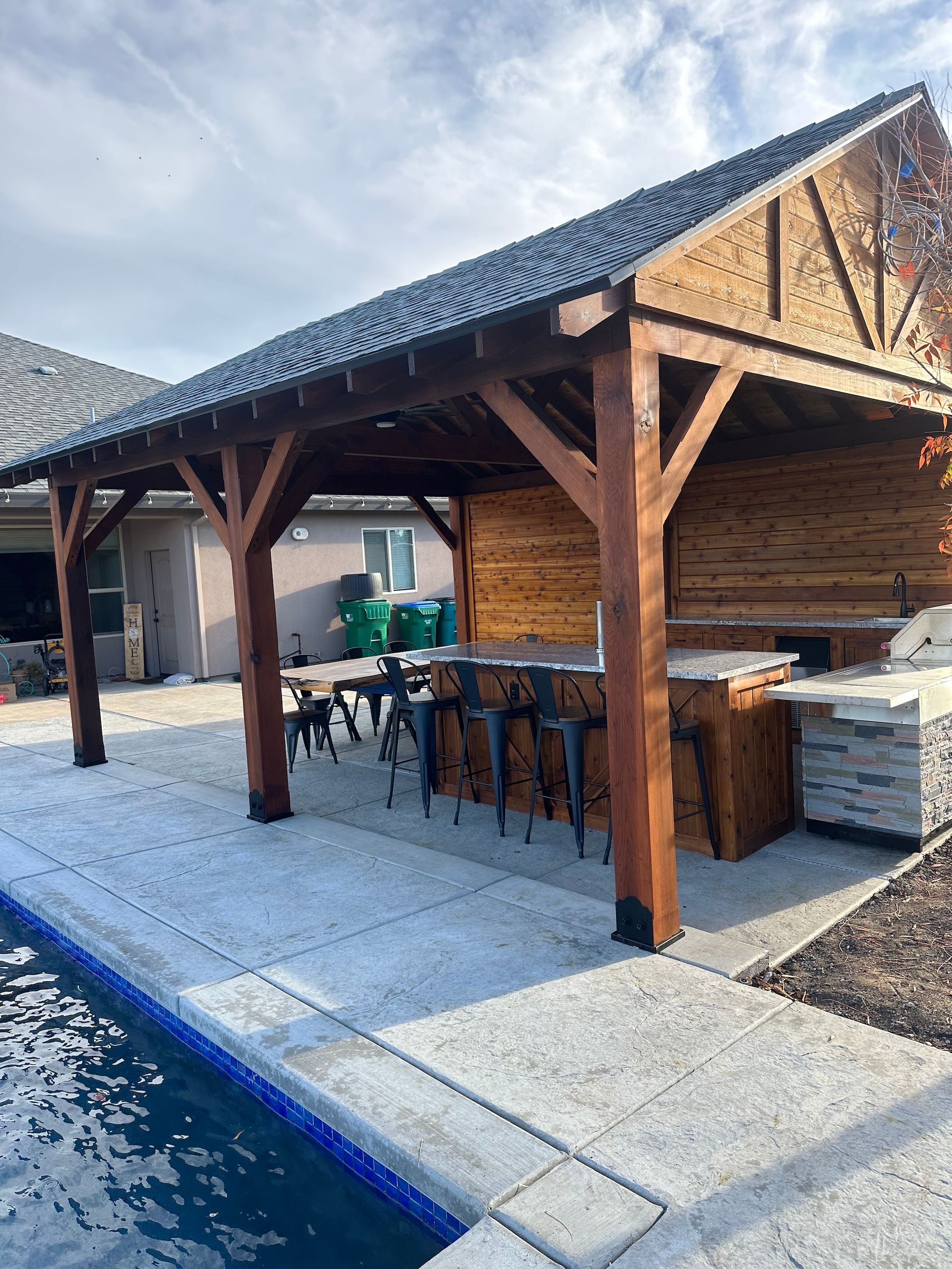 a wooden pavilion with a bar and stools next to a swimming pool .
