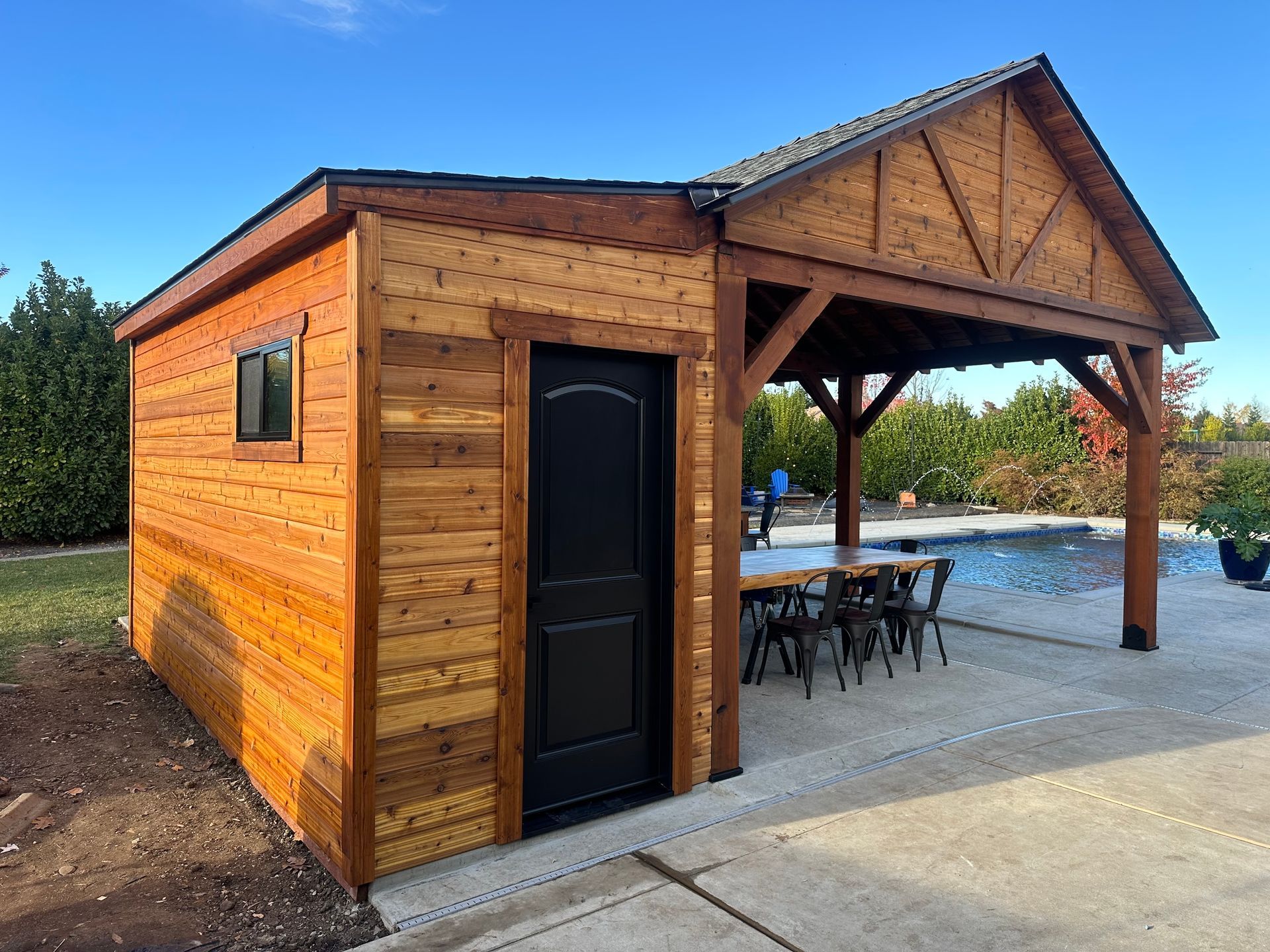 a wooden shed with a table and chairs underneath it next to a pool .