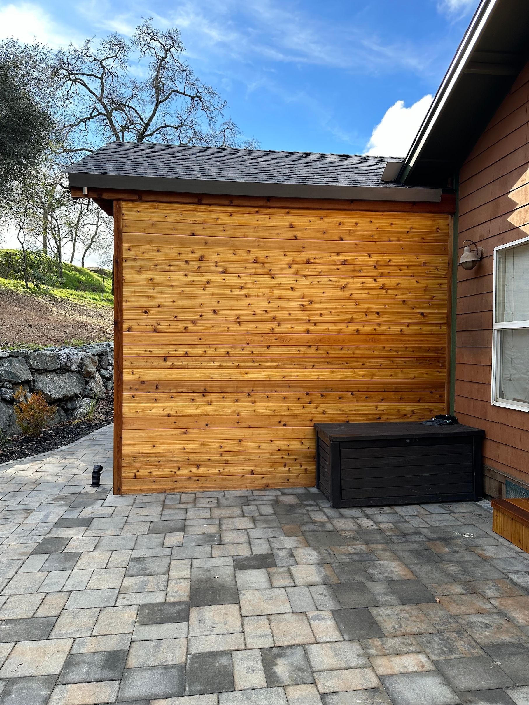 a wooden shed is sitting on a brick patio next to a house .