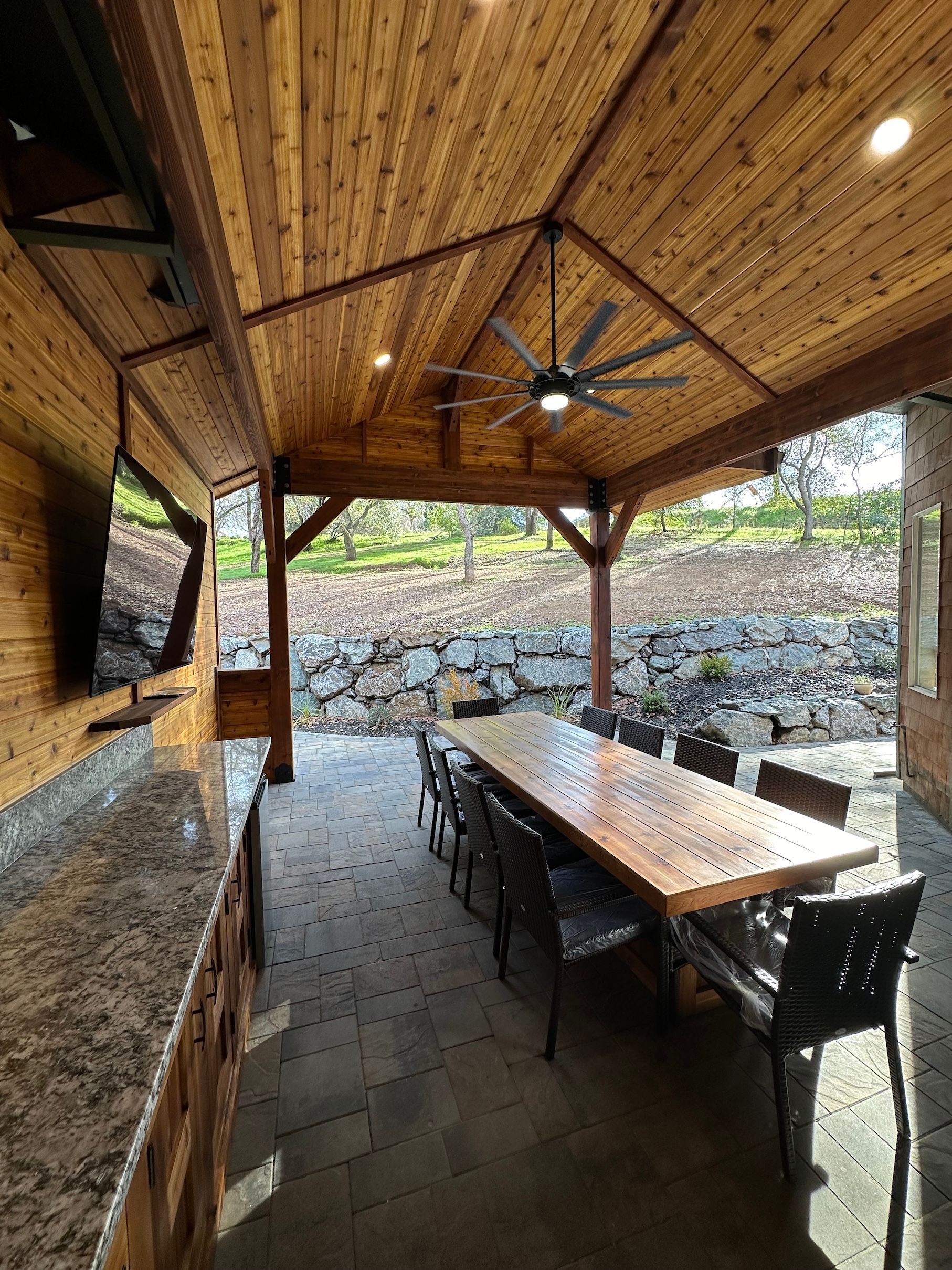 a large wooden table and chairs under a wooden ceiling with a ceiling fan .