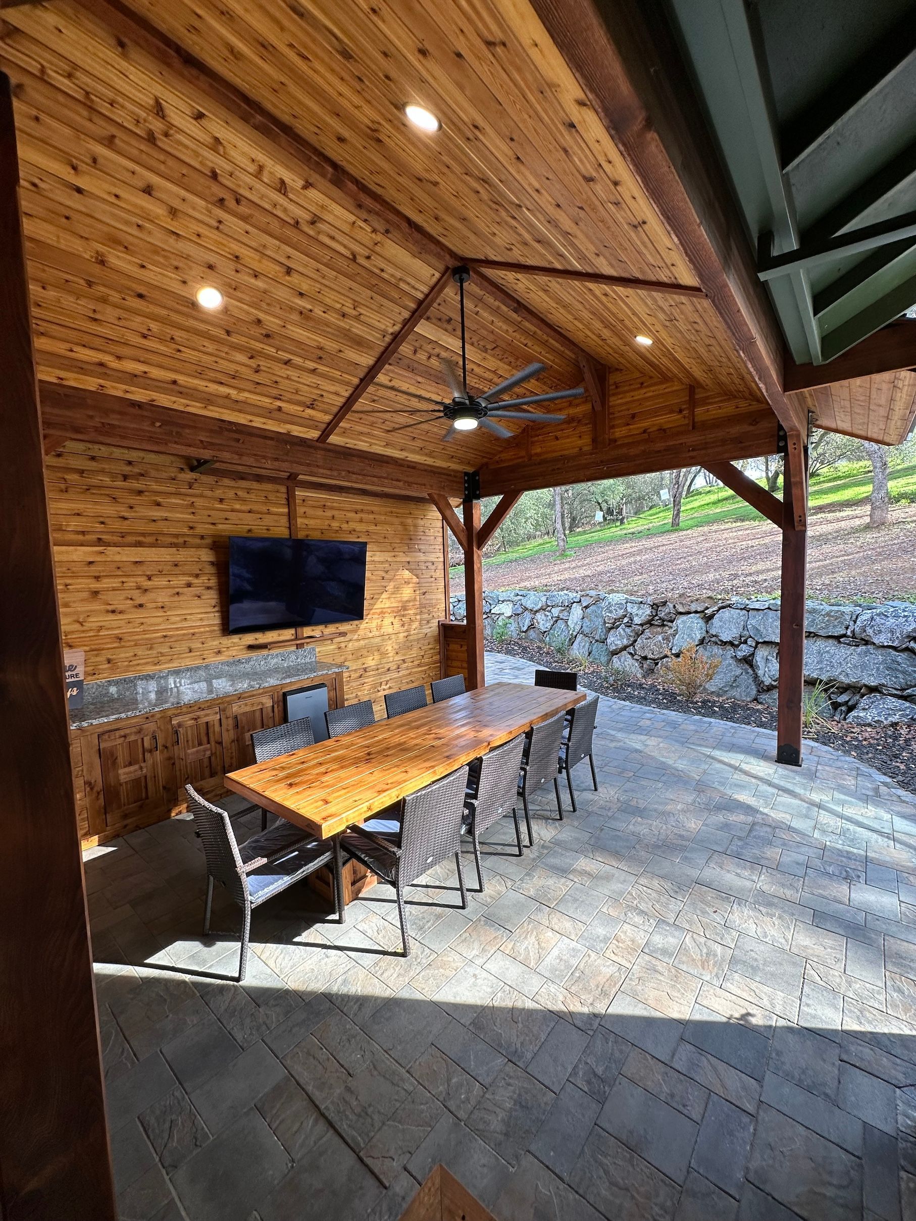 a covered patio with a long wooden table and chairs and a flat screen tv .